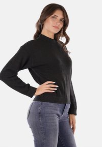 Maglione nero a collo alto, con maniche lunghe e orlo a coste, realizzato in un morbido tessuto testurizzato, abbinato a jeans blu.