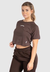 Brun kortermet t-shirt med et hvidt logo på fronten. Matcher med brune joggerbukser med elastisk talje.