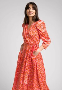 Jasnopomarańczowa sukienka o kroju wrap z zabawnym wzorem z różowymi akcentami, trzyczwarte rękawy i kieszenie po obu stronach. Gładka tekstura materiału.
