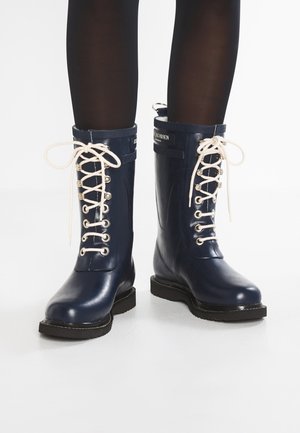 Bottes de pluie en caoutchouc navy avec une finition brillante, lacets blancs, œillets en métal et semelle noire. Présente un logo en haut de l'arbre.
