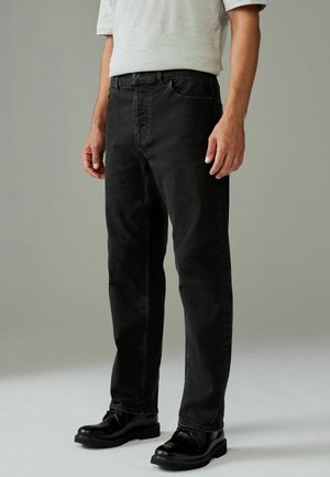 Zwarte denim jeans met een rechte pasvorm, riemlussen en een vijf-pocket ontwerp. Draagt een lichtgrijze shirt met korte mouwen en zwarte laarzen.