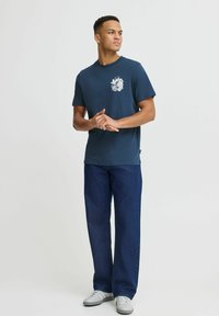 Mörkblå bomullströja med ett vitt blommigt mönster på bröstet, tillsammans med vida jeanstights och grå sneakers.