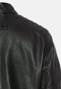 Sort læderjakke med quiltet skulderdesign og lille trykknaplukning. Teksturen er glat med en blød glans.