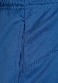 Blått tyg i närbild av idrottsshorts som visar en slät textur, elastisk midja, sidoficka och rena sömmar.