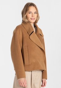 Brązowa kurtka z mieszanki wełny z szerokim kołnierzem, dwurzędowym zapięciem i dużymi bocznymi kieszeniami. Miękka tekstura i luźny krój.