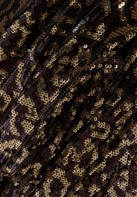 Zwarte stof versierd met gouden en bronzen pailletten in een luipaardprintpatroon, met een getextureerd, glanzend oppervlak.