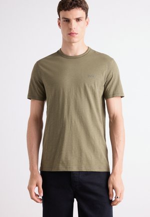 Olive green short-sleeve T-shirt in soft fabric with a crew neckline and a small, discreet logo on the left chest. Styled with dark jeans.