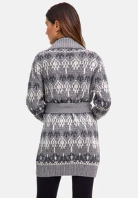 Długi szary kardigan z białym wzorem. Posiada kołnierz szalowy, pasek do przewiązania oraz prążkowane mankiety i dół dla dodatkowej faktury.