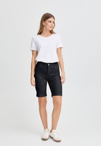 Shorts in denim nero con vita alta e orlo arrotolato, abbinati a una t-shirt in cotone bianca aderente. Include scarpe da ginnastica bianche. Design semplice.
