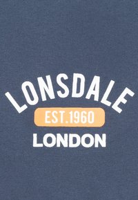 Tamno plavi materijal s bijelim tekstom: "LONSDALE" zakrivljen iznad i "LONDON" ispod, s narančastim pravokutnikom koji navodi "EST. 1960" u podebljanim slovima.