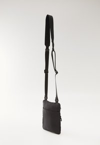 Black fabric crossbody bag with adjustable strap, rectangular shape, zippered front pocket, and smooth texture.
