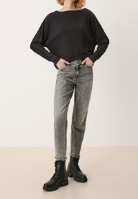 Svart långärmad topp med vid halsringning, kombinerad med ljusgrå högmidjade jeans. Svarta kängor med snörning och tjock sula.