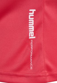 Rød atletisk skjorte med en glat tekstur, prydet med hvid "hummel PERFORMANCE" logo langs venstre side. Simpelt design, ingen mønstre.