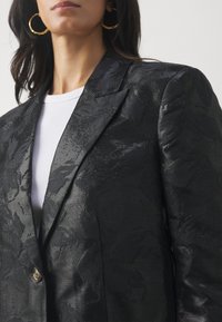 Svart blazer med et strukturert blomsterdesign, med en slank silhuett, notched lapels og en enkelt knappelukking.