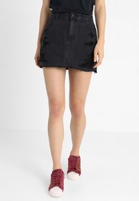 Černá džínsová mini sukně s odřenými detaily, třepeným lemem a přiléhavým střihem. V kombinaci s červenými teniskami s bílou podrážkou.