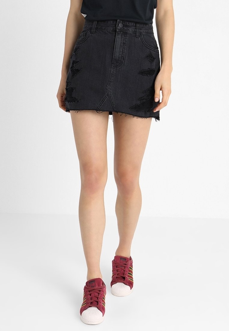 Černá džínsová mini sukně s odřenými detaily, třepeným lemem a přiléhavým střihem. V kombinaci s červenými teniskami s bílou podrážkou.