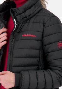 Sort puffervest med quiltet tekstur. Har røde logoaccenter på venstre bryst og højre ærme. Høj krave og lynlåslukning.