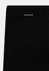 Pantaloni neri con una texture liscia, dotati di una tasca frontale e un piccolo accento a righe rosse e bianche in vita.