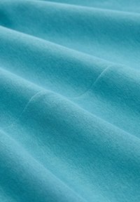 Turquoise stof met een gladde textuur, voorzien van zachte plooien en een gelijkmatige kleurverdeling, die de lichtgewicht en ademende eigenschappen benadrukt.