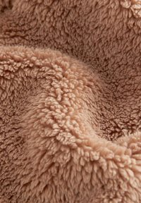 Piumoso e morbido plaid di un leggero beige, con una superficie spessa e texture densa, caratterizzata da fibre arricciate e un aspetto accogliente.
