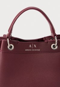 Sac à main en cuir bourgogne avec quincaillerie en argent, doté d'une anse supérieure et d'un logo embossé. Fini texturé et œillets ronds sur le haut.