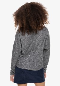 Suéter gris de punto con un patrón texturizado, de ajuste holgado y brazos caídos, combinado con una falda de pana azul oscura.