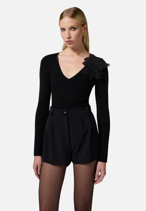 Body aderente nero a costine con scollatura a V profonda e un dettaglio di pizzo a forma di fiore sulla spalla sinistra, abbinato a pantaloni corti neri a vita alta.