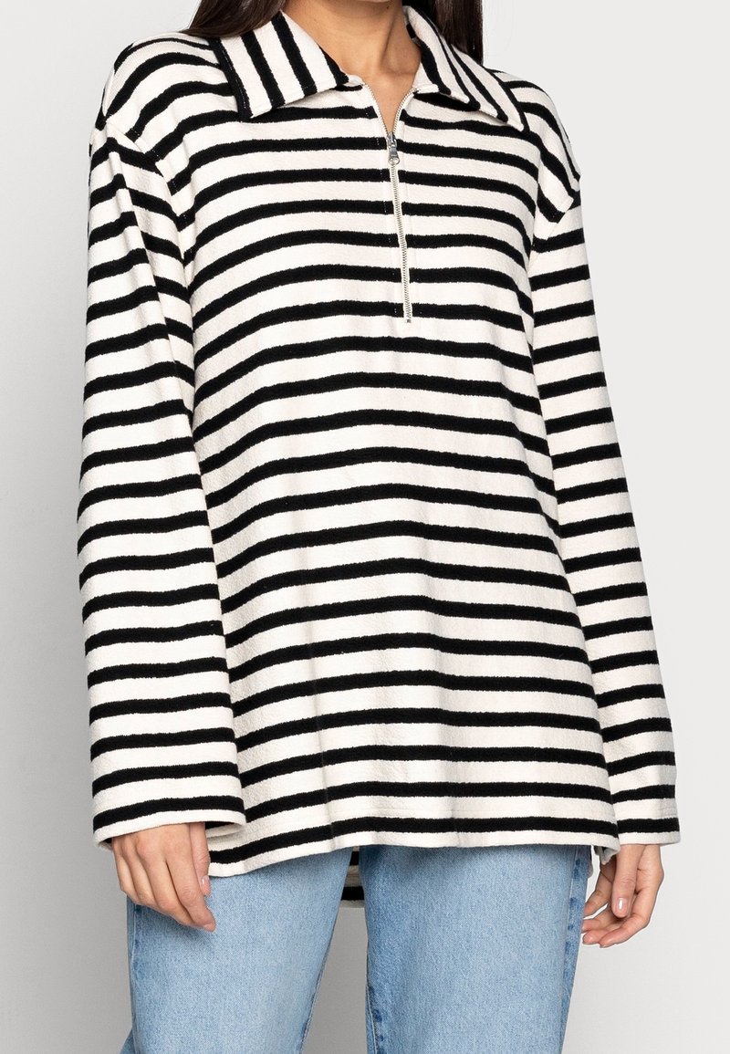 Randig pullover i svart och vitt med krage, halvdragkedja fram och långa ärmar. Tillverkad av ett strukturerat tyg, har den en avslappnad passform.