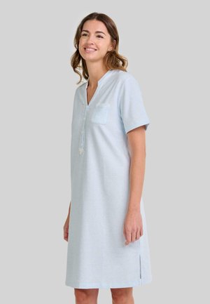 Mujer sonriendo, vistiendo un vestido de manga corta hasta la rodilla de color azul claro con botones en el frente, bolsillo en el pecho y abertura lateral, contra un fondo liso.
