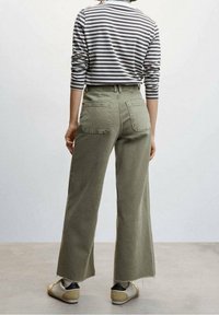 Olijfgroene wijde broek met achterzakken, gecombineerd met een grijs-wit gestreept shirt met lange mouwen. Textuur van katoen.