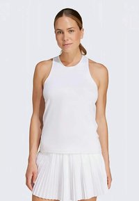 Valge tank top kõrge kaelusega ja ilma varrukateta, valmistatud siledast kangast. Kombineeritud volangidega valge seelikuga.