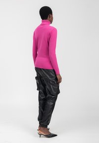 Fuchsia Rollkragenpullover kombiniert mit schwarzen Leder-Cargo-Hosen und spitzen schwarzen High Heels. Glatte Textur, figurbetontes Design und lange Ärmel.