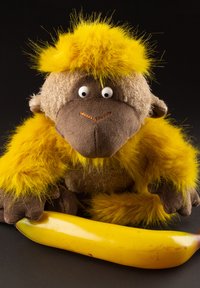 Stuffed monkey toy with bright yellow fur holding a ripe yellow banana against a black background.