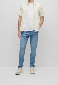 Košile s krátkým rukávem se žlutými a bílými pruhy, doplněná jednoduchým bílým tričkem a světle modrými džínami. Dokončeno béžovými teniskami.