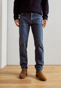 Donkerblauwe denim jeans met een rechte pijp, voorzien van een subtiele vervaagde textuur, voorzakken en een decoratieve patch op de tailleband.