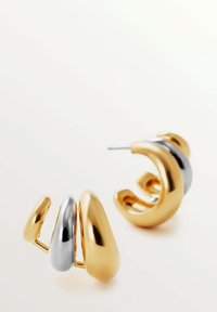 Pendientes de oro y plata con un diseño suave y redondeado en diferentes tamaños. Un pendiente tiene un acento plateado brillante entre las curvas de oro.