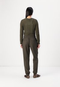 Olivgrön stickad tröja med texturerade mönster, ihopparad med matchande byxor med elastisk midja och läderskor i leopardmönster.