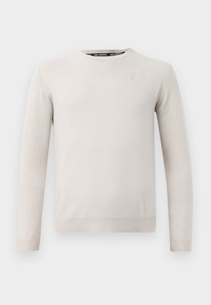 Lys beige genser laget av mykt stoff, med rund hals, lange ermer og ribbede mansjetter og nederkant. Diskret logo detalj på brystet.