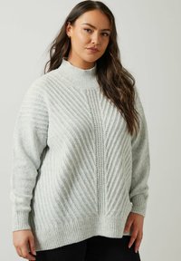 Lichtgrijze gebreide trui met een hoge hals, voorzien van diagonaal geribbeld textuur en een subtiele opengehaakte paneel in het midden. Losse pasvorm.