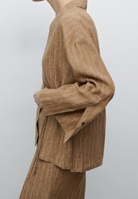 Veste en lin rayée marron avec une coupe décontractée, dotée d'un col et de boutons décoratifs, assortie d'une jupe. Texturée et légère.
