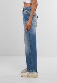 Gaiši zili, augsta jostas lieluma džinsi ar taisnu piegriezumu, ar aizmugurējām kabatām un kontrastējošām šuvēm. Kombinēti ar baltām kedām.