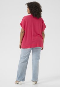 Maglietta oversized fucsia con maniche corte, in tessuto leggero, abbinata a jeans a gamba dritta azzurri e sandali bianchi con tacco.