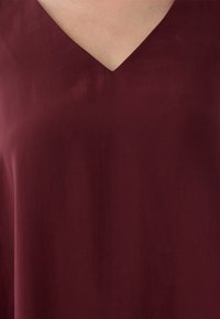 Burgundowa bluzka z dekoltem w kształcie litery V. Miękka tkanina o gładkiej fakturze. Prosty design bez wzorów czy ozdób.
