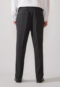Dunkelgraue maßgeschneiderte Hose mit geradem Bein, ausgestattet mit Gesäßtaschen und einer glatten Textur, kombiniert mit schwarzen Schuhen.