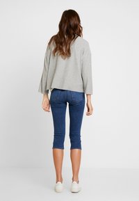 Grå kortärmad tröja med vida ärmar, parat med mörkblå tajta jeans och vita sneakers, sett bakifrån.