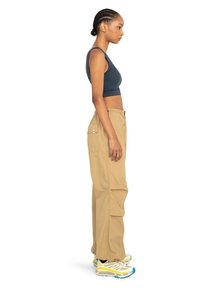 Ciemnoniebieski crop top, luźne beżowe spodnie cargo z bocznymi kieszeniami i kolorowe buty do biegania z niebieskimi i żółtymi akcentami.