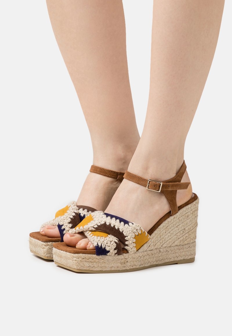 Sandales compensées marron avec accents en tissu coloré et talon en jute tressé. Elles présentent une bride avec fermeture à boucle et un design tissé texturé.