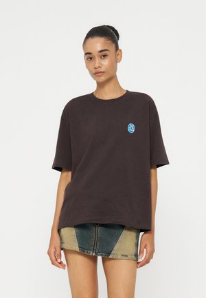 Jonge vrouw draagt een donker oversized T-shirt met een klein blauw logo en een tweekleurige denim minirok met een rits aan de voorkant.