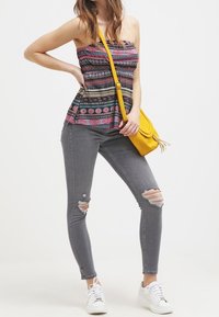 Top sin tirantes con estampado en negro, rosa y blanco; combinado con unos vaqueros ajustados rasgados en gris y zapatillas blancas; complementado con un bolso cruzado amarillo.