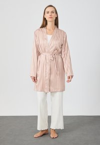 Roze satijnen kimono met verticale strepen, strikceintuur in de taille, lange mouwen, tot op de knie. Gecombineerd met witte broeken met geschulpte zoom.